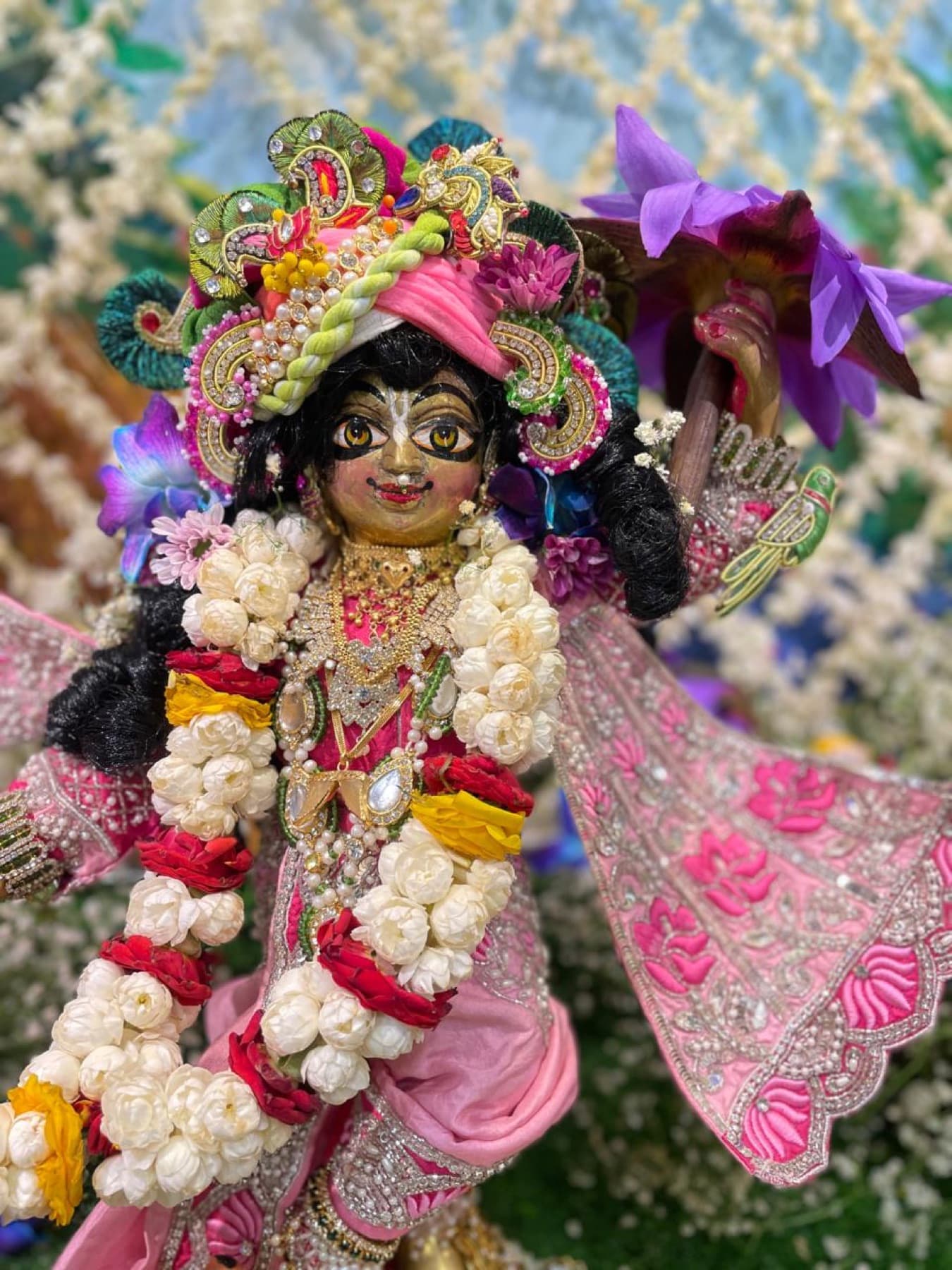 Krishna deity dressed in a hand-embroidered pink poshak, garlanded with flowers